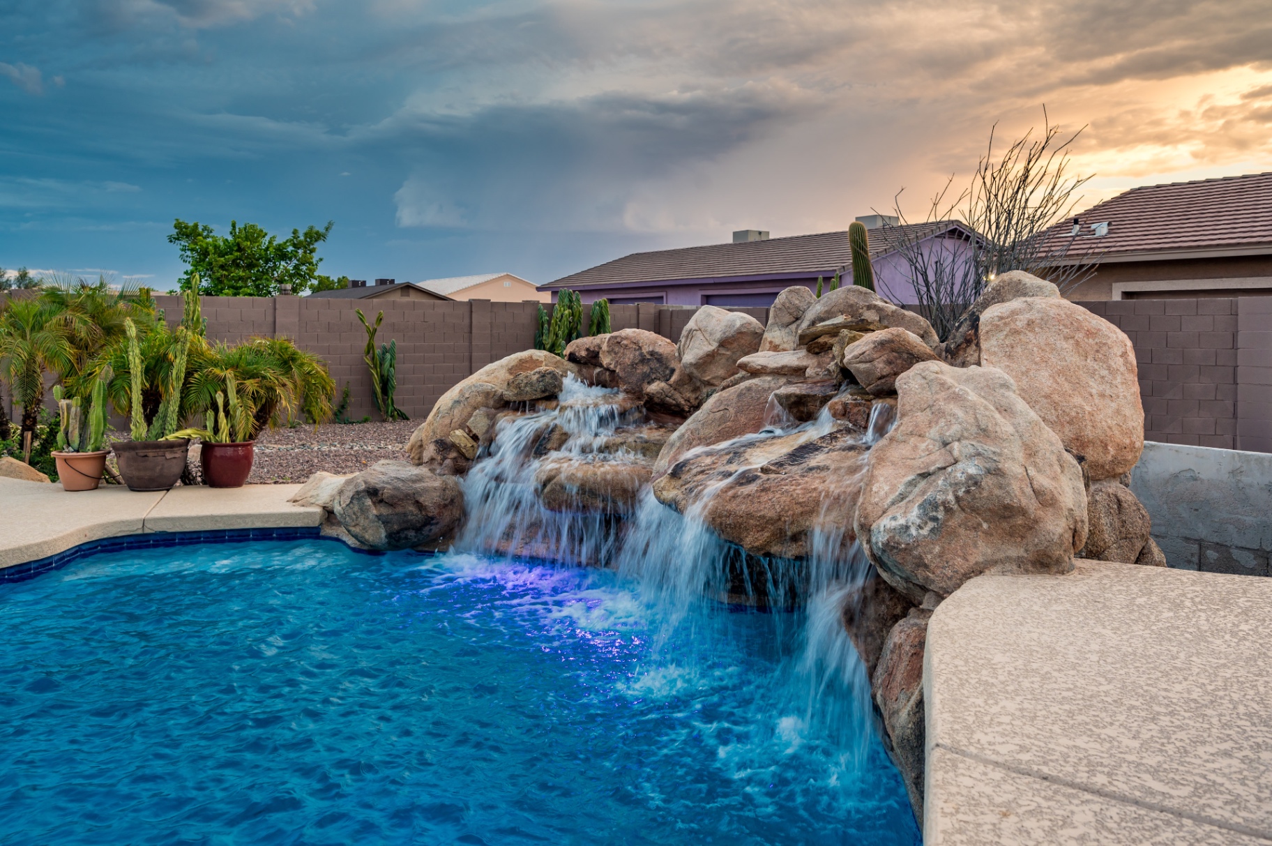 Pool grotto waterfall illuminated at sunset with desert plants