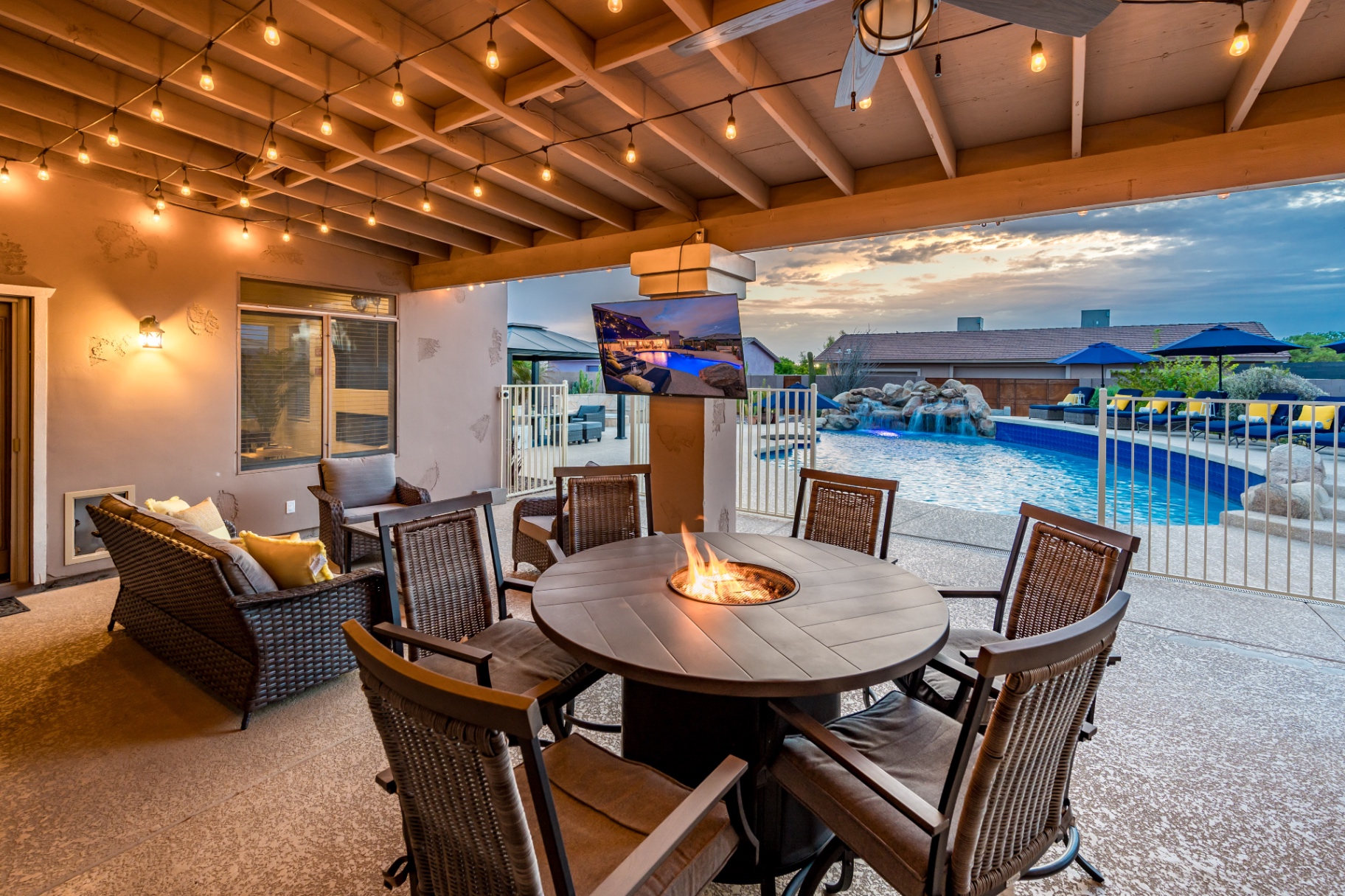 Covered patio fire pit table at dusk with TV and pool views