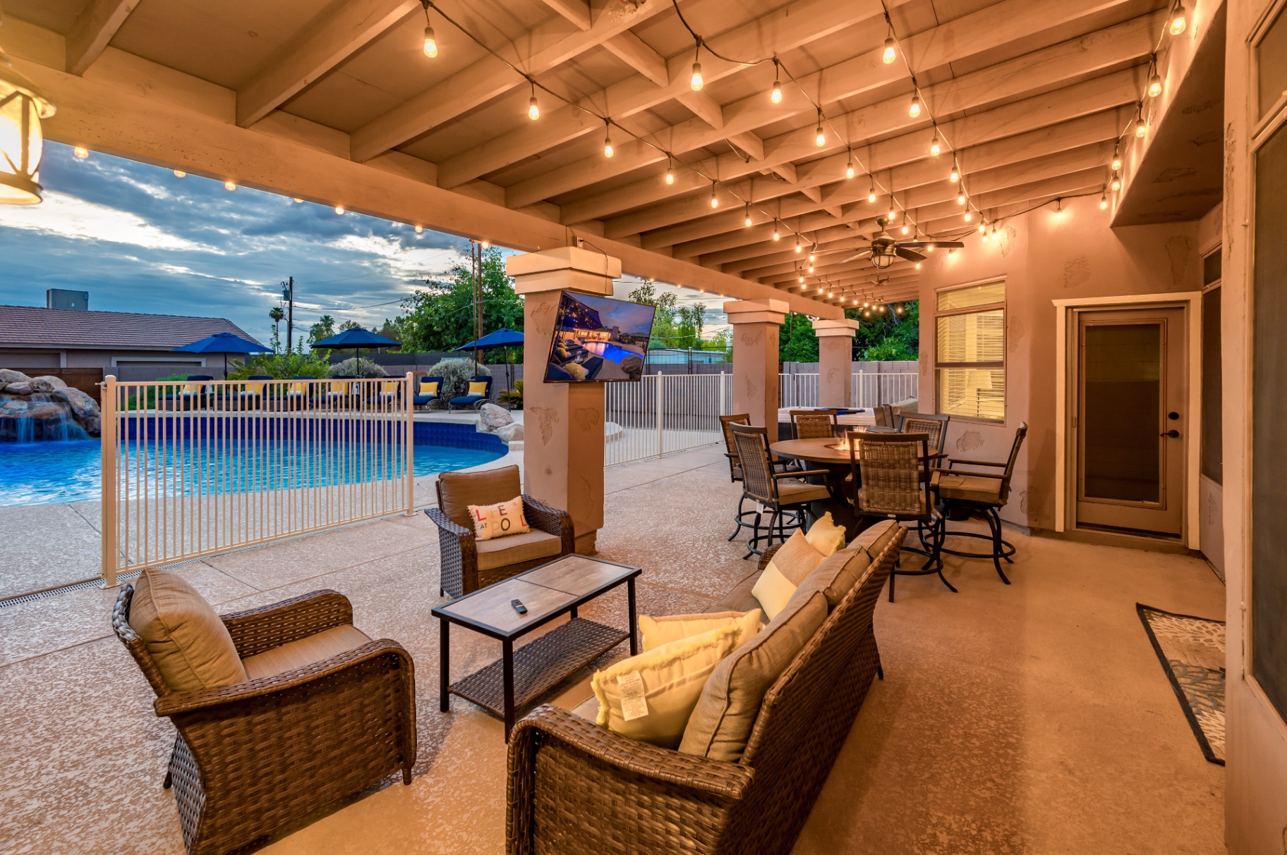 String-lit patio lounge and dining area beside the pool at twilight