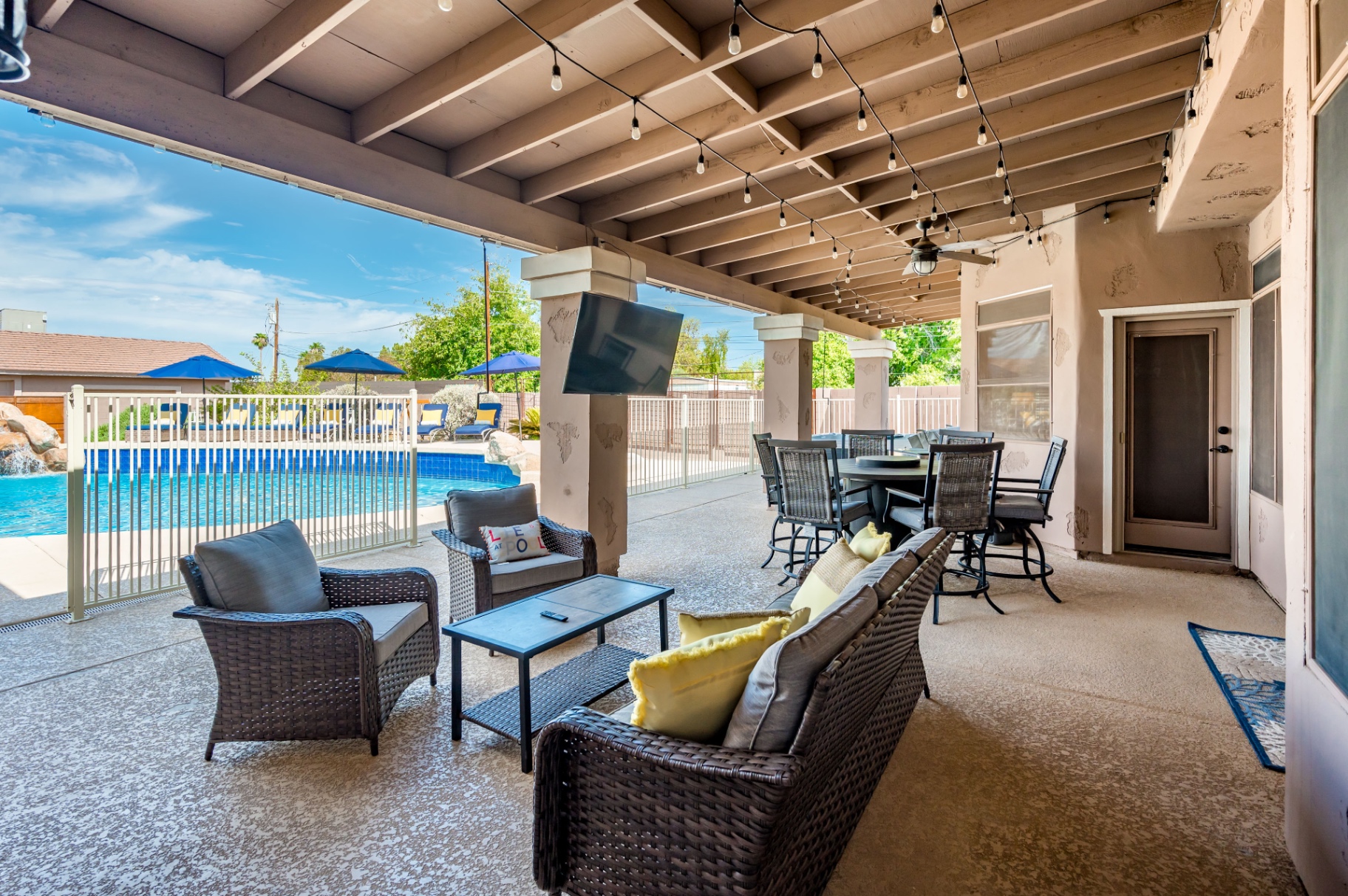Covered patio lounge with TV, dining set and string lights overlooking the pool